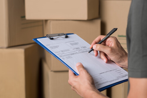Boxes in the background while a person fills out a delivery form. 