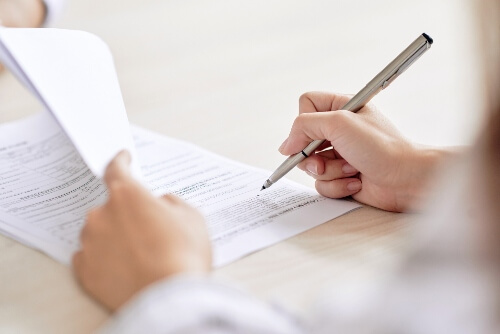 A hand holding a pen hovers over legal papers ready to sign and process them.