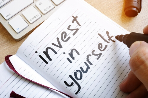 A notepad below a keyboard has the words invest in yourself written on it.